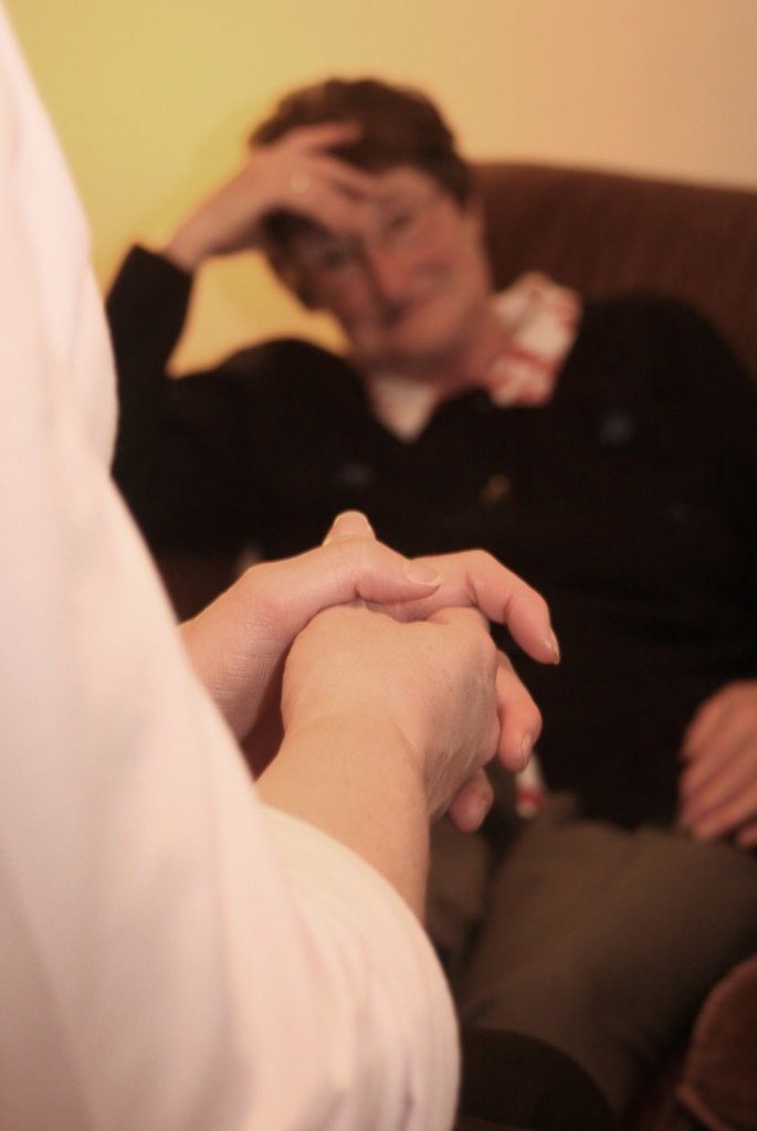 A caregiver gently holds a person's hands during a quiet, supportive conversation.