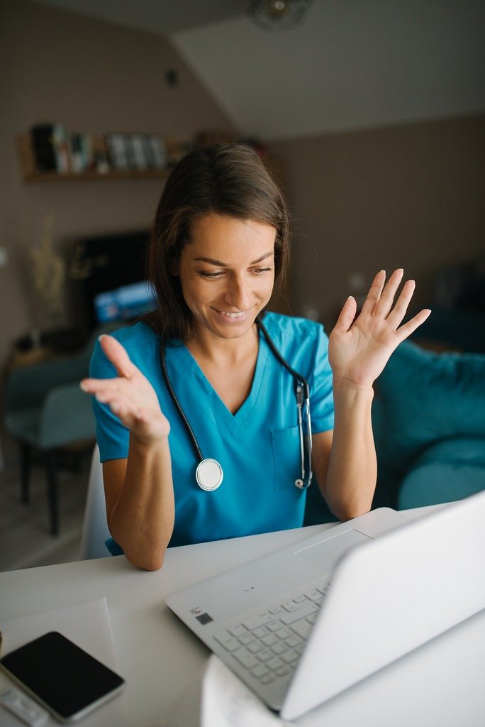 A clinician smiles while speaking with someone over a secure video call on a laptop.